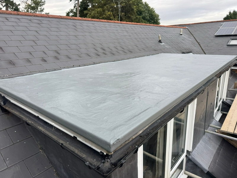 A professionally repaired GRP flat roof extension featuring a seamless Concrete Grey waterproof coating and new high-performance guttering.