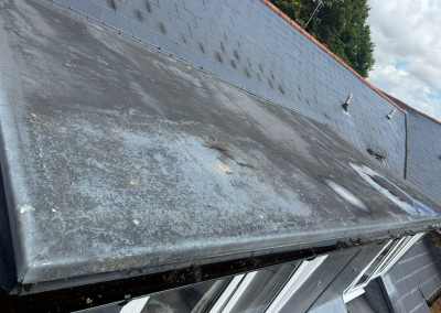 A damaged GRP flat roof edge showing significant cracking and standing water in a blocked gutter, requiring professional roofing repair.