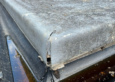 A damaged GRP flat roof edge showing significant cracking and standing water in a blocked gutter, requiring professional roofing repair.