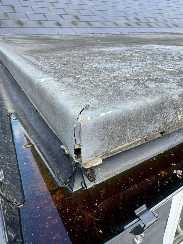 A damaged GRP flat roof edge showing significant cracking and standing water in a blocked gutter, requiring professional roofing repair.