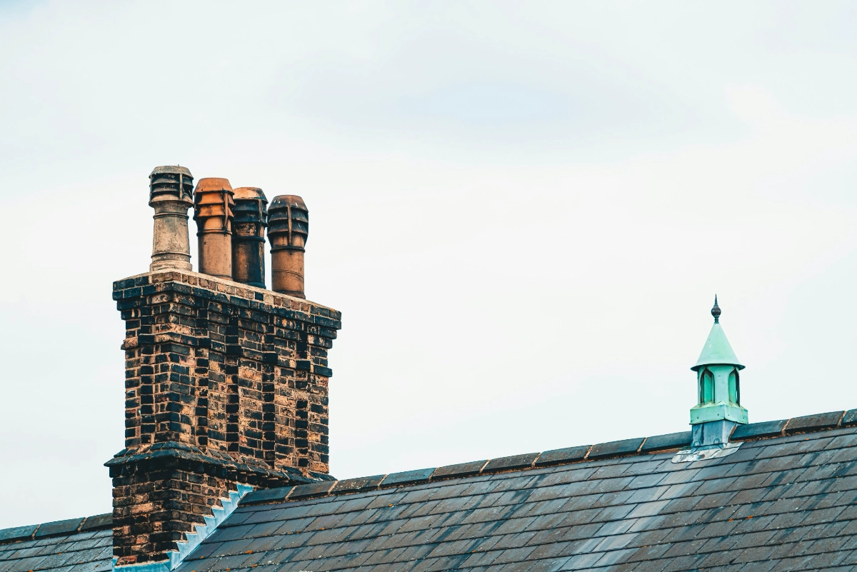 Restored heritage brick chimney stack and traditional slate roof featuring a decorative lead finial, demonstrating FRR Midlands Ltd’s specialist preservation work.