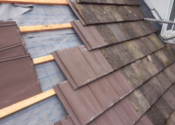 Professional roofers performing a partial tile replacement on a residential property, showing the installation of new durable tiles alongside weathered heritage roofing