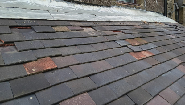 Uneven roof tiles beneath lead flashing at the junction with an exterior wall.